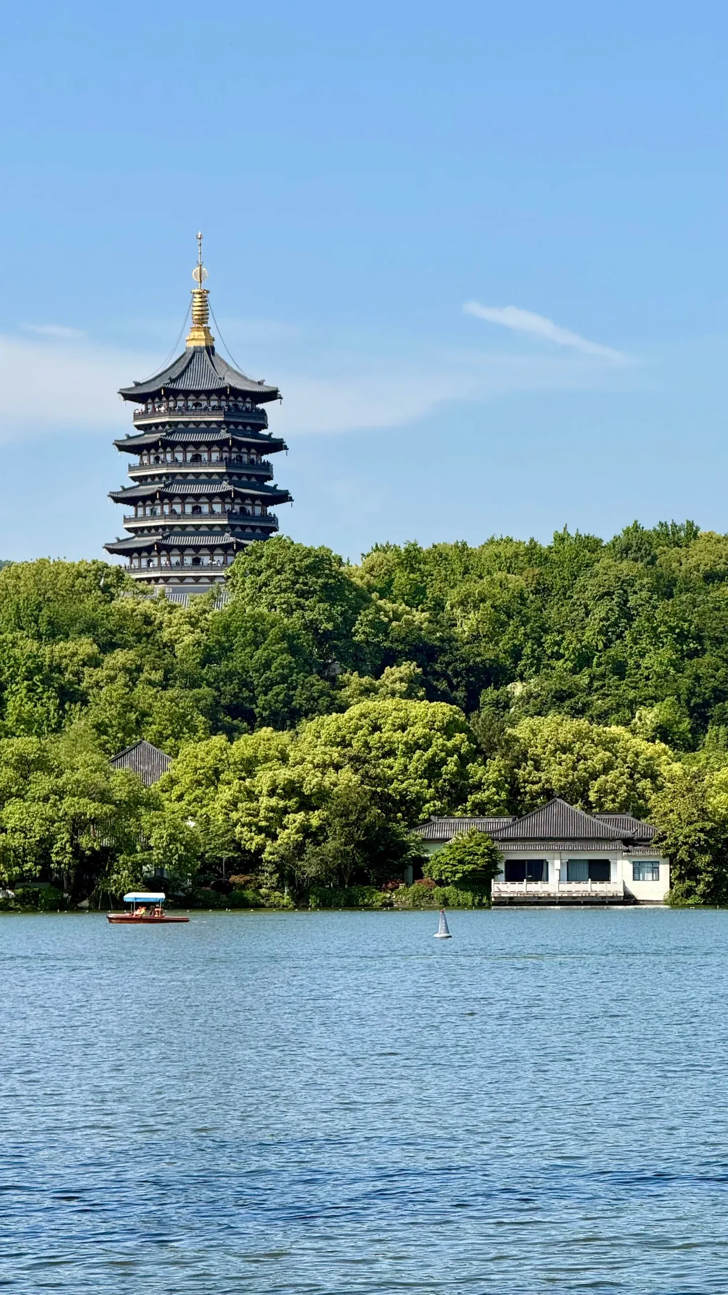 Leifeng Pagoda rising out of dense trees above West Lake, with a small boat on the water.