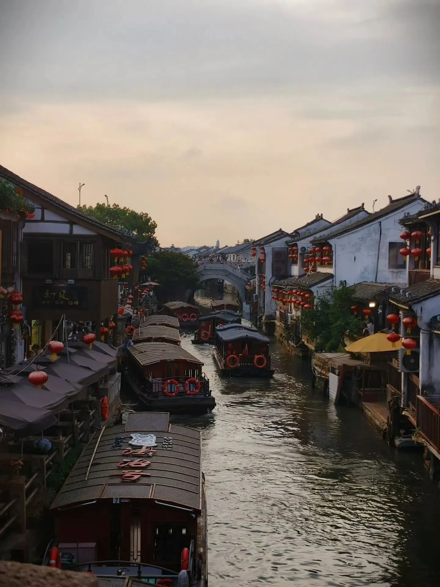 Tour boats and red lanterns lining the canal through Yuehe Ancient Town in Jiaxing at dusk.